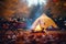 Camping site with fire lit in fire pit in Autumn woods with beautiful Fall foliage colors. Autumn seasonal concept.