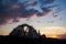 Camping at sunset in the mountains. The tent stands on grass with wildflowers under evening sky