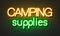 Camping supplies neon sign on brick wall background.