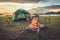 Camping tent with bonfire in the green field meadow, Lake and mountain background. Picnic and travel concept. Nature theme