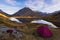 Camping with tent near high altitude lake on the Alps. Reflection of snowcapped mountain range and scenic colorful sky at sunset.