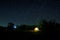 Camping tent under beautiful night sky full of stars. Starry night sky above illuminated touristic tent