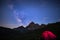 Camping under starry sky and milky way at high altitude on the Alps. Illuminated tent in the foreground and majestic mountain peak