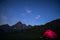 Camping under starry sky and milky way at high altitude on the Alps. Illuminated tent in the foreground and majestic mountain peak