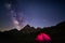 Camping under starry sky and milky way at high altitude on the Alps. Illuminated tent in the foreground and majestic mountain peak