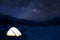 Camping in the wilderness. A pitched tent under the glowing night sky stars of the milky way with snowy mountains. Milky Way and M