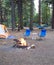 Campsite in the woods with a tent,two chairs, hammock and a burning firepit.