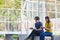 On a campus, a couple of students are studying together, and a teenager sits on a seat beside a sports court with a book