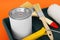 Can of orange paint, brushes, roller and container on color background, closeup