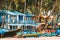 Canacona, Goa, India. Fishing Boat And Famous Painted Guest Houses On Palolem Beach Against Background Of Tall Palm