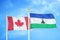 Canada and Lesotho two flags on flagpoles and blue cloudy sky