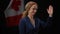 Canadian politician woman smiling waving looking away at black background with national flag. Confident diplomat posing