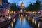 Canal with bridge, cathedral and boats in evening Amsterdam. Traditional dutch cityscape in twilight.