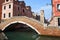 Canal and bridge in quieter area of Venice with wall and tower of the Arsenale .