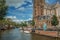 Canal with old brick steeple church, boats and sunny blue sky in Amsterdam.