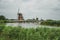 Canal with tall bushes, bridge and windmills on the bank in a cloudy day at Kinderdijk.