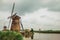 Canal with tall bushes, bridge and windmills on the bank in a cloudy day at Kinderdijk.