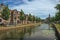 Canal with trees, aquatic plants, brick houses and church on sunny day in Weesp.