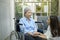 Cancer patient woman wearing head scarf sitting on wheelchair talking to her supportive daughter indoors, health and insurance