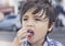 Candid head shot of cute little boy eating condy floss with blurry  street background, Young boy with deep in though while eating