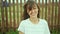 Candid image brunette woman smiling to camera and looking happy, standing by wooden fence on background.