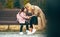 Candid image of mother and her girl kid smiling, sitting on a bench outdoors. Loving joyful young woman and her happy daughter