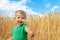 Candid portrait of cute adorable caucasian blond little toddler boy enjoy walking in ripe golden wheatfield giving wheat
