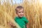 Candid portrait of cute adorable caucasian blond little toddler boy enjoy walking in ripe golden wheatfield looking