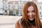 Candid Portrait of happy beautiful cheerful smiling laughing redhead girl looking at camera over blurred city background with copy