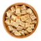 Candied ginger root cubes in wooden bowl over white