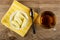Candies in shape of bananas in bowl, spoon on napkin, cup with tea on wooden table. Top view