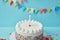 Candle on birthday cake with sugar sprinkles on blue background