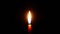 The candle burns in the darkness with a bright flame. Light on a black background