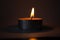 Candle on dark luxury night background. Black table, side view. Candles Burning at Night. Orange taper burning in focus,