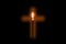 Candle is glowing through hole in shape of Christian cross