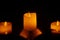 The candle glows orange in the black darkness.  There is reflection, concept, religious prayer, peace, advent