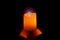 The candle glows orange in the black darkness.  There is reflection, concept, religious prayer, peace, advent