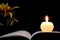 Candle, opened book and flowers isolated on black