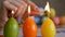 Candles made in shape of easter egg. Green, orange, yellow. Female hand lights candles.