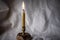 Candlestick with a burning candle on the background of rumpled linen fabric. Dark vignette