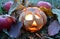 Candlestick pumpkin with burning candle inside, among autumn fallen leaves and red apples, symbol of Halloween