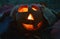 Candlestick pumpkin with a burning candle inside, among fallen leaves in the dark, symbol of Halloween