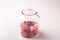 Candy canes sweets in form of juicy berries in glass jar on white wooden background