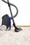 Canister modern vacuum cleaner blue for cleaning the house on the background of the wall and soft carpet.