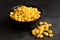 Canned sweet corn in a black ceramic bowl isolated on black slate next to spilled sweet corn