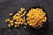 Canned sweet corn in a black ceramic bowl isolated on black slate next to spilled sweet corn. Top view