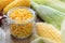 Canned sweet corn in glass jar, fresh and cooked corn cobs.