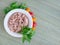 Canned tuna fillet in white porcelain bowl, parsley and some cherry tomatoes on a green table mat made of natural plant fibers.