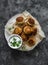 Canned tuna potato fish balls with greek yogurt cilantro sauce on dark background, top view