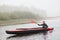 Canoe on lake with beautiful bushes on background. Foggy panorama with male paddler padding on cold water, man canoeing alone,